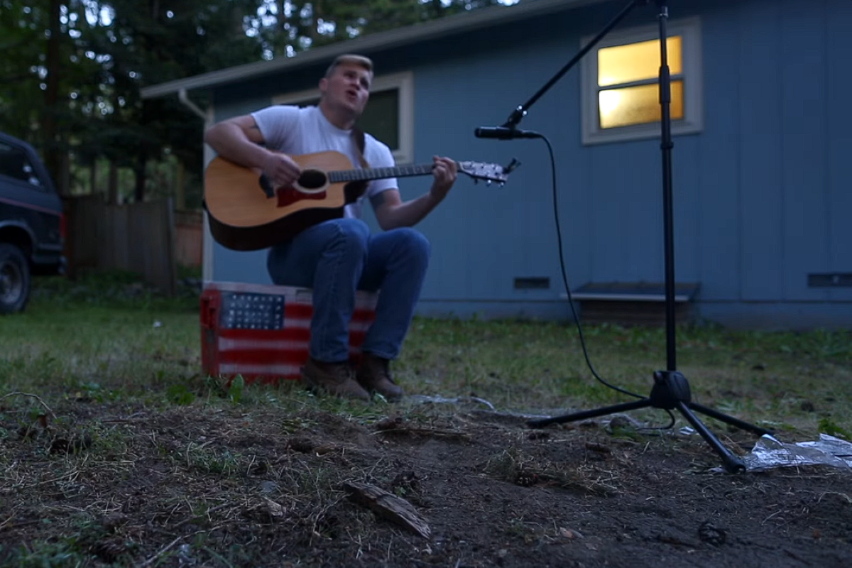 zach bryan singing and playing guitar outside