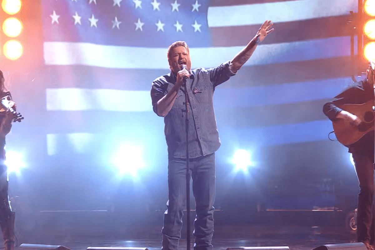 Blake Shelton singing with an American flag behind him